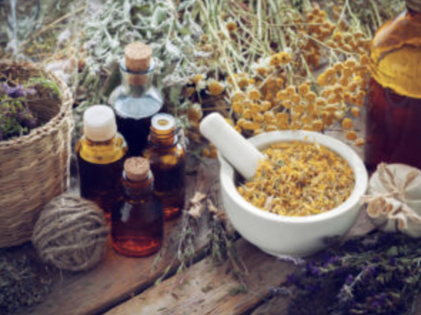 Amber bottles of herbal tinctures beside a mortar and pestle of dried chamomile flowers and bundles of dried herbs